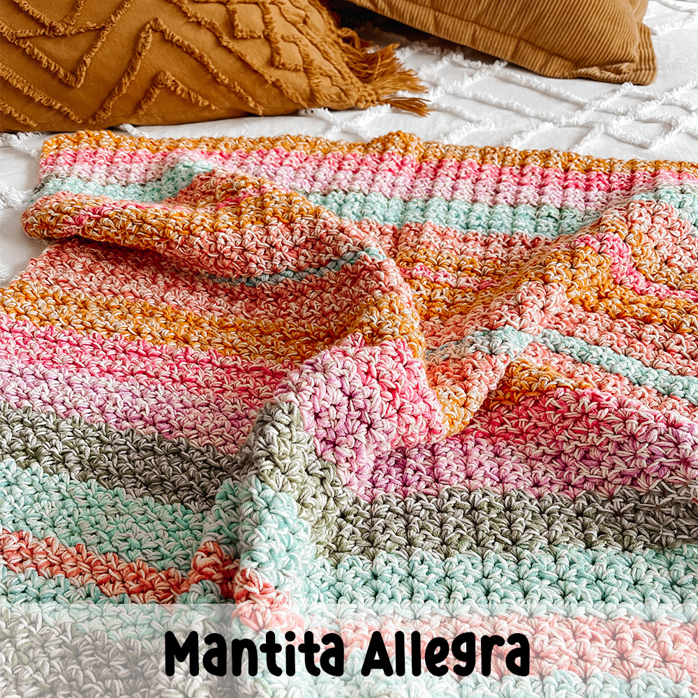 an image of a colourful crochet blanket, laid on a white bed with a couple of mustard pillows in the back.